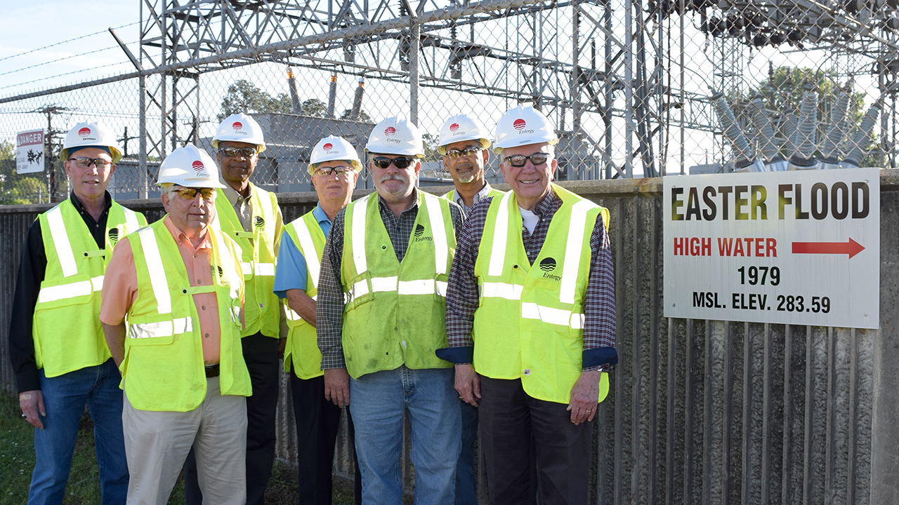 A group of employees and retirees who worked during the Easter Flood of 1979 gather at the Northeast Jackson Substation where a marker indicates how high the water level rose at that facility. From left Ed Smith, senior customer service representative, meter reading operations, Bob Hawkins, retiree, Louis Wright, customer service representative, Ken Coleman, retiree, Bill Bailey, serviceman, Darek Ashley, operations coordinator, and Don Meiners, retiree.